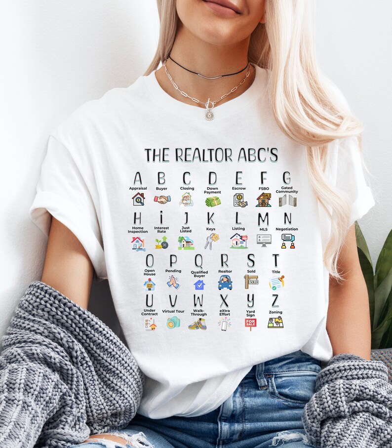 May include: White t-shirt with a black graphic of the alphabet with real estate related terms and icons. The text reads "THE REALTOR ABC'S".