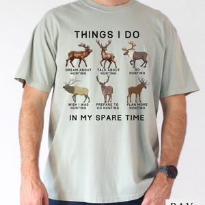 May include: A light sage green short-sleeve t-shirt featuring a graphic with six different deer illustrations and the text: THINGS I DO, DREAM ABOUT HUNTING, TALK ABOUT HUNTING, GO HUNTING, WISH I WAS HUNTING, PREPARE TO GO HUNTING, PLAN MORE HUNTING, IN MY SPARE TIME.