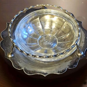 Könnte beinhalten: Eine Vintage-Servierschale versilbert mit einem durchsichtigen Glaseinsatz. Die Schale hat einen gewellten Rand und einen Griff. Der Glaseinsatz hat ein geriffeltes Design. Die Schale wird wahrscheinlich zum Servieren von Butter oder anderen Gewürzen verwendet.
