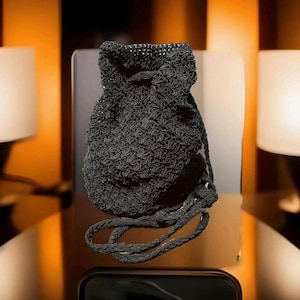 Puede incluir: Una bolsa de cordón de crochet negro con una larga correa trenzada negra.
