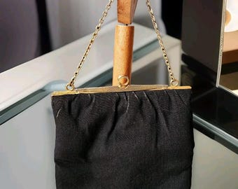 Puede incluir: Un bolso de noche negro vintage con un marco y una cadena de metal dorado. El bolso está hecho de una tela texturizada y tiene forma rectangular. La cadena es delicada y el marco tiene un cierre de broche.