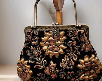 Può includere: Borsa a mano in stile vintage con esterno in velluto nero, ornata da ricami floreali dorati. La borsa presenta una montatura in metallo, un manico e una chiusura a scatto. Il design floreale è dettagliato con piccole perline.