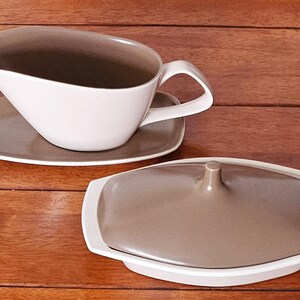 May include: A two-piece serving set with a gravy boat and a covered dish. The gravy boat is white with a brown interior and sits on a matching saucer. The covered dish is white with a brown lid. Both pieces have a mid-century modern design.