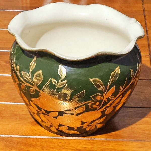Pode incluir: Um vaso decorativo de cerâmica com exterior verde escuro e interior branco. O vaso apresenta desenhos de folhas e galhos dourados. A borda tem uma borda ondulada.