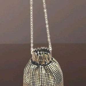 Könnte beinhalten: Eine goldene Netz-Zugschnurtasche mit einer Kettenkette. Die Tasche besteht aus kleinen, quadratischen Metallteilen.