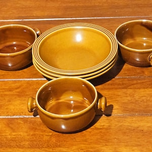 May include: A set of brown ceramic bowls and dishes. The set includes four small bowls with handles, and a stack of four larger, shallow bowls. The bowls have a glossy finish and are arranged on a wooden surface.