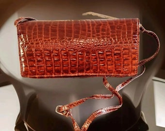 May include: A brown leather crossbody bag with a crocodile embossed pattern. The bag has a long strap and a flap closure.