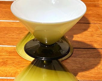 Może przedstawiać: Trzy kieliszki do koktajli w stylu vintage. Kieliszki mają unikalny design z białym wnętrzem i zielonym zewnętrzem, które przechodzi od ciemniejszej zieleni u podstawy do jaśniejszej zieleni u góry. Nóżka jest czarna. Kieliszki stoją na drewnianej powierzchni.