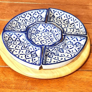 Puede incluir: Una fuente para servir con base de madera y cinco cuencos de cerámica blancos y azules. Los cuencos tienen un estampado floral y están dispuestos en forma circular. La base de madera es de color marrón claro.