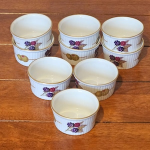 May include: A collection of eight white ceramic ramekins with a gold rim and a decorative pattern of purple blackberries, red raspberries, and green leaves. The ramekins have a ribbed design and a painted olive design. Ideal for baking and serving individual portions.