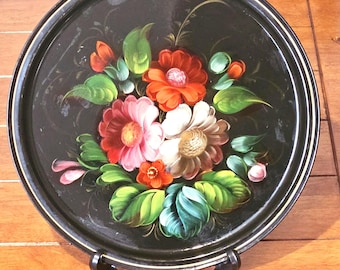 May include: Round black tray with a floral design. The tray features a bouquet of red, pink, and white flowers with green leaves. The rim has a gold accent. The tray is displayed on a black stand.