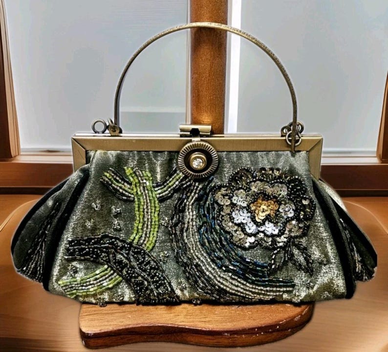 May include: An olive green handbag with a gold-toned frame and handle. The bag is decorated with beaded and sequined floral and abstract designs in green, black, and gold. The clasp has a central jewel.
