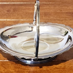 Puede incluir: Una cesta de servir plateada con asa. La cesta ovalada tiene un borde festoneado y se asienta sobre una base redonda. El asa se arquea hacia arriba, completando el elegante diseño. Ideal para servir pasteles o pequeños artículos.