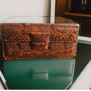 Peut inclure: Une pochette en cuir de serpent brun avec un détail de nœud décoratif.