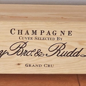 May include: A light-colored wooden champagne box with the words "CHAMPAGNE" and "Berry Bros. & Rudd Ltd" printed in black. The box also has the words "CUVEE SELECTED BY" and "GRAND CRU" printed on it.