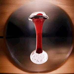 Peut inclure: Un vase en verre rouge avec une base en verre clair. Le vase a un sommet unique et bulbeux et un long col fin.