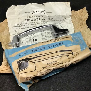 May include: A chrome trigger latch with installation instructions from Stanley Hardware. The packaging includes a blue and tan paper with the words "Blue Ribbon Designs" and "Actual Size".