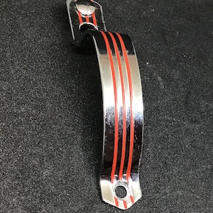 May include: A chrome door handle with three red stripes. The handle is curved and has a rounded top and bottom.