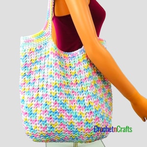May include: A large, colorful crochet tote bag with a chevron pattern in shades of pink, blue, yellow, and white. The bag is being held by a model, and the text "CrochetnCrafts" is visible in the bottom right corner.
