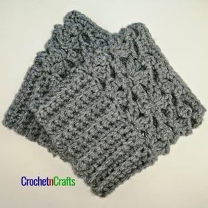 May include: Grey crocheted fingerless gloves with a lacy pattern on the top of the hand. The gloves are folded in half and the crocheted fabric is visible.