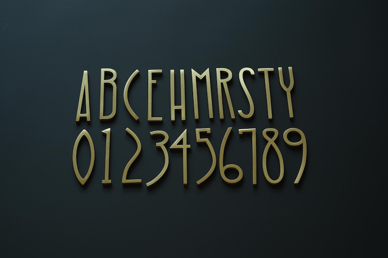 K&ouml;nnte beinhalten: Goldfarbene Metallbuchstaben und -zahlen, einschlie&szlig;lich A bis Y und 0 bis 9, sind auf einer dunkelgrauen Oberfl&auml;che angeordnet. Die Buchstaben und Zahlen haben eine elegante, moderne Schriftart.