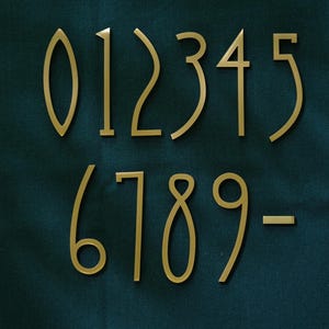 K&ouml;nnte beinhalten: Ein Satz goldfarbener Hausnummern, einschlie&szlig;lich der Zahlen 0 bis 9 und eines Bindestrichs. Die Zahlen sind in einer modernen Schriftart gehalten und vor einem dunkelblauen Hintergrund dargestellt.