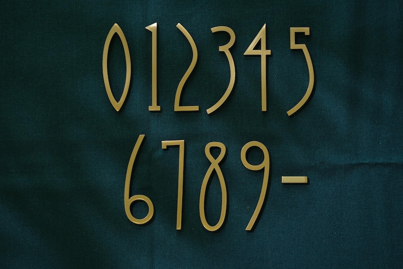 K&ouml;nnte beinhalten: Ein Satz goldfarbener Hausnummern, einschlie&szlig;lich der Zahlen 0 bis 9 und eines Bindestrichs. Die Zahlen sind in einer modernen Schriftart gehalten und vor einem dunkelblauen Hintergrund dargestellt.