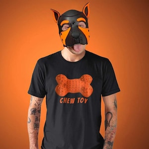 May include: A person wearing a black t-shirt with an orange chew toy graphic and the text "CHEW TOY". The person is also wearing a black and orange dog mask.