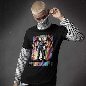 Könnte beinhalten: Schwarzes T-Shirt mit einem Aufdruck eines gehörnten Dämons mit Flügeln, der vor einem Regenbogenhintergrund steht. Der Text "PRIDEMONTH" ist unter dem Aufdruck gedruckt.