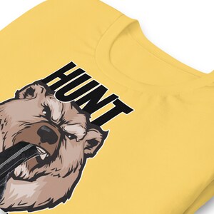 May include: Yellow t-shirt with a brown bear graphic and the word "HUNT" in black text.