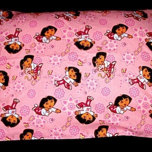 May include: Pink pillowcase with a repeating pattern of a cartoon character wearing a purple shirt and red pants. The character is surrounded by pink flowers and stars.