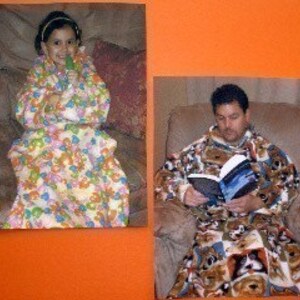 May include: Two people wearing colorful fleece blankets with sleeves. The person on the left is a child wearing a blanket with a floral pattern. The person on the right is an adult wearing a blanket with a dog pattern. Both people are sitting in chairs.