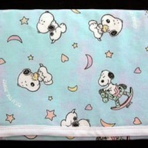 May include: A light blue baby blanket with a white border. The blanket features a repeating pattern of Snoopy characters, stars, hearts, and crescent moons.