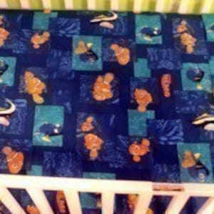 May include: A blue and orange crib sheet with a Finding Nemo theme. The sheet features a repeating pattern of Nemo, Dory, and other characters from the movie.