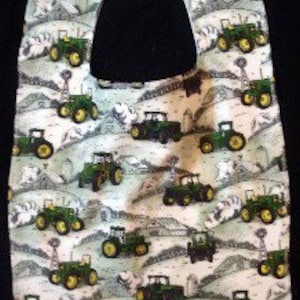 May include: A green and white baby bib with a tractor pattern. The bib has a large opening for the head and a smaller opening for the neck.