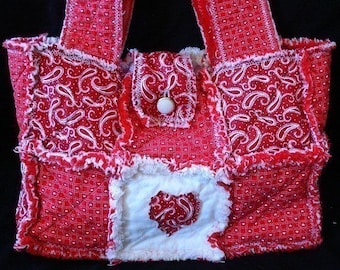 Puede incluir: Bolso tote de patchwork rojo y blanco con un diseño en forma de corazón. El bolso tiene un cierre de botón blanco y un borde deshilachado.