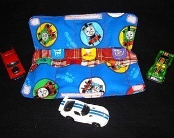 May include: Blue fabric toy organizer with a Thomas the Tank Engine print. The organizer has three pockets and is filled with toy cars. The cars are red, green, and white.