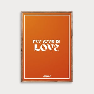 May include: A framed art print with an orange background and white text that reads "I'VE BEEN IN LOVE" in a bold, retro font. The word "JUNGLE" is at the bottom. The frame is a natural wood color.