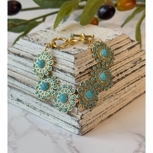 May include: A gold bracelet with turquoise blue flower-shaped charms. The bracelet has a clasp closure.