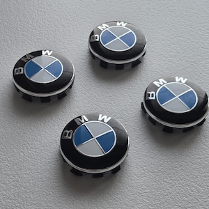 Op de afbeelding: Vier zwarte en zilveren BMW wieldopjes met het BMW-logo. Het logo heeft een blauw en wit gesegmenteerde cirkel met de BMW-letters rond de rand. De doppen liggen op een grijze ondergrond.
