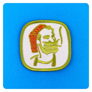 Könnte beinhalten: Grüner gestickter Aufnäher mit weißem Hintergrund, der ein Cartoon-Bild eines Mannes mit Bart und einem roten und orangen Stirnband zeigt. Das Stirnband trägt den Text "Old Man Doom".