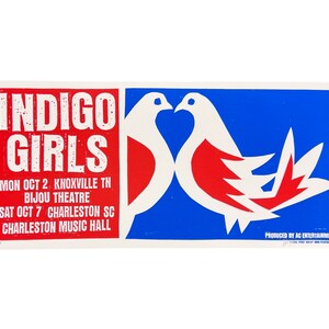 May include: A concert poster for Indigo Girls with a red, white, and blue color scheme. The poster features two white doves with red accents facing each other. The text on the poster reads "Indigo Girls" in white letters on a red background. The dates and locations of the concerts are listed below the band name.