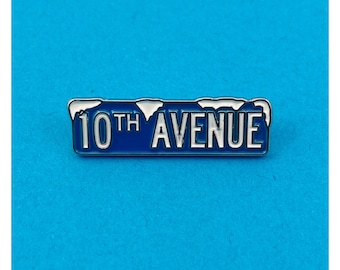 May include: A blue and silver enamel pin with the text "10th AVENUE" in white lettering. The pin has a snowy design on top.