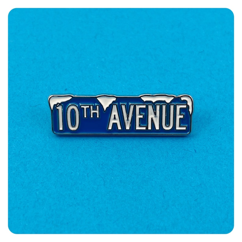 May include: A blue and silver enamel pin with the text "10th AVENUE" in white lettering. The pin has a snowy design on top.