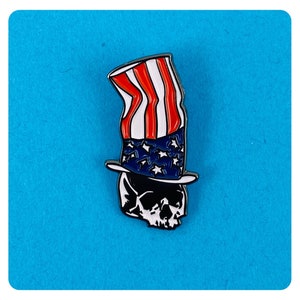 May include: A black and white enamel pin of a skull wearing a red, white, and blue Uncle Sam hat.