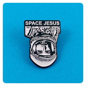 May include: Black and white enamel pin featuring an astronaut with the text "SPACE JESUS" above the astronaut's head.