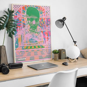 Pode incluir: Um p&ocirc;ster emoldurado com um design psicod&eacute;lico rosa e verde que apresenta um retrato de uma pessoa com o rosto verde e um len&ccedil;o estampado em rosa e branco. O p&ocirc;ster tem o texto "The Machine" na parte inferior.