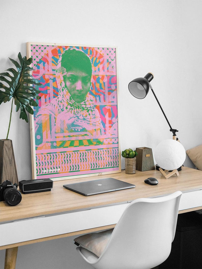 Pode incluir: Um p&ocirc;ster emoldurado com um design psicod&eacute;lico rosa e verde que apresenta um retrato de uma pessoa com o rosto verde e um len&ccedil;o estampado em rosa e branco. O p&ocirc;ster tem o texto "The Machine" na parte inferior.