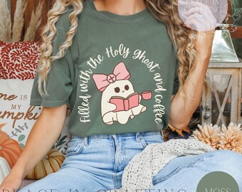 Op de afbeelding: Een groen T-shirt met een schattige geestillustratie die een boek en een kopje koffie vasthoudt. De tekst op het shirt luidt "Filled with the Holy Ghost and coffee".