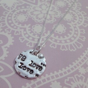 May include: A silver necklace with a round pendant that says "We love... Love". The pendant has a textured surface and the words are embossed.